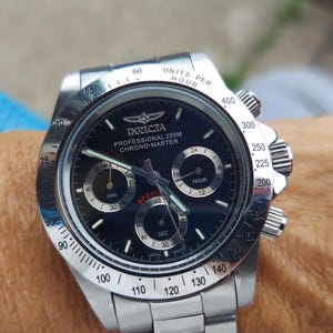 May include: A stainless steel Invicta Professional 200M Chrono-Master watch with a black dial. The watch features sub-dials, a tachymeter bezel, and the Invicta logo. The watch is on a stainless steel strap.