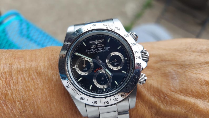 May include: A stainless steel Invicta Professional 200M Chrono-Master watch with a black dial. The watch features sub-dials, a tachymeter bezel, and the Invicta logo. The watch is on a stainless steel strap.