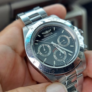 May include: A stainless steel Invicta Professional 200M Chrono-Master watch with a black dial. The watch features three sub-dials, luminous hands, and a date display. The watch has a stainless steel band and a rotating bezel.
