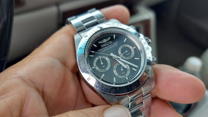 May include: A stainless steel Invicta Professional 200M Chrono-Master watch with a black dial. The watch features three sub-dials, luminous hands, and a date display. The watch has a stainless steel band and a rotating bezel.