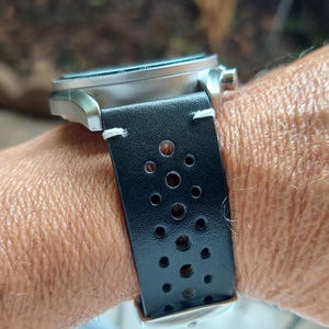 Pu&ograve; includere: Un orologio da polso con cassa in metallo argento spazzolato e cinturino in pelle nera. Il cinturino &egrave; traforato con una serie di piccoli fori circolari disposti a motivo ed &egrave; fissato con cuciture bianche visibili vicino alle anse.