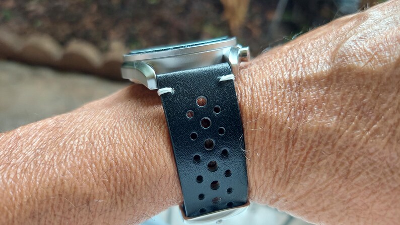 Pu&ograve; includere: Un orologio da polso con cassa in metallo argento spazzolato e cinturino in pelle nera. Il cinturino &egrave; traforato con una serie di piccoli fori circolari disposti a motivo ed &egrave; fissato con cuciture bianche visibili vicino alle anse.