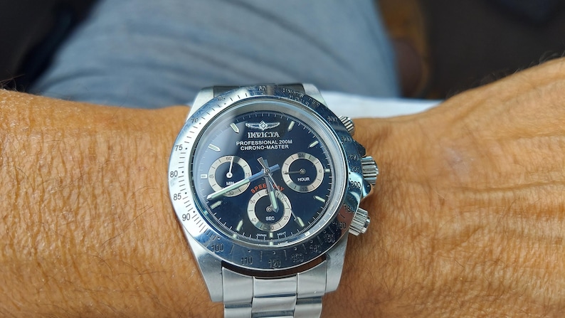 May include: A silver Invicta Professional 200M Chrono-Master watch with a dark blue face. The watch has three sub-dials, a date display, and a silver bezel with white markings. The watch is on a silver metal band.