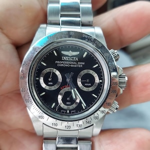 May include: A stainless steel Invicta Professional 200M Chrono-Master watch with a black dial. The watch features three sub-dials, a rotating bezel, and a stainless steel band. The watch has a diameter of approximately 4.5 cm.