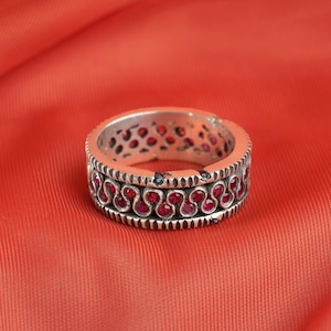 Puede incluir: Un anillo de plata con una banda de piedras preciosas rojas engastadas en un patrón decorativo.