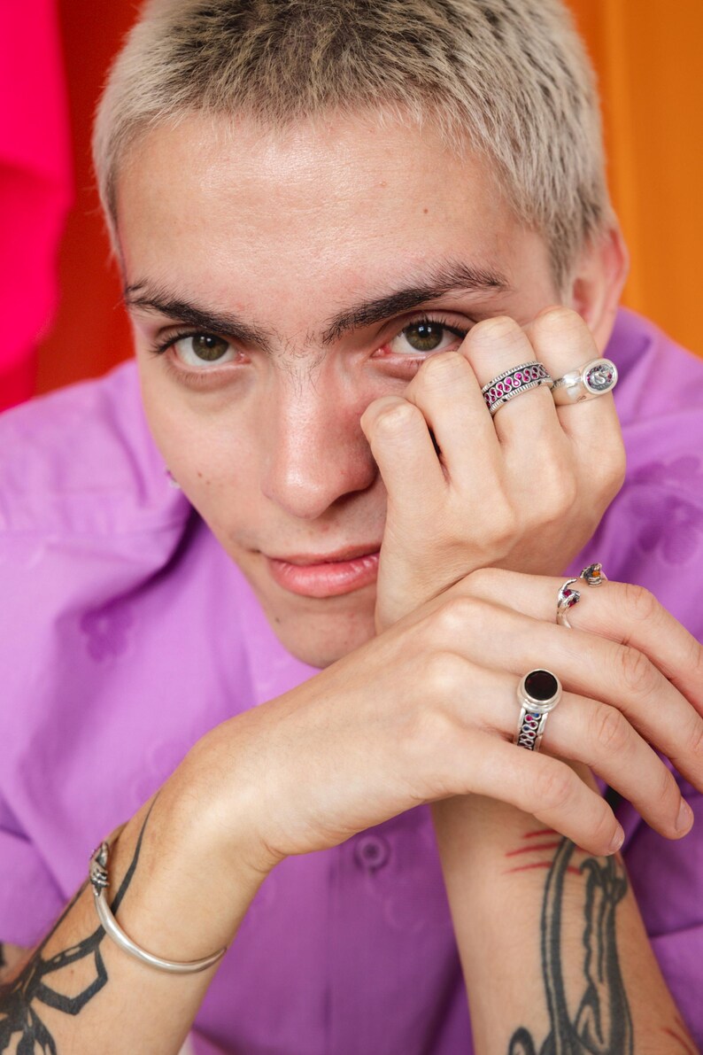 May include: A person wearing a purple shirt with silver rings on their fingers. The person has short, light blonde hair and is looking down.