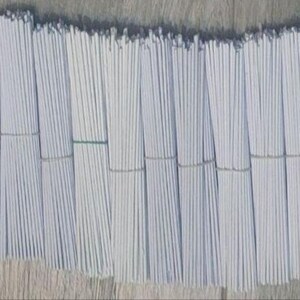 Peut inclure: Plusieurs paquets de bâtonnets blancs et fins, attachés avec de fines bandes de couleur claire. Les bâtonnets sont disposés en rangées ordonnées, créant une apparence uniforme. Le fond est une surface en bois brun clair.