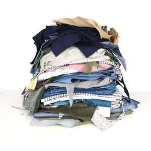 May include: A large pile of fabric scraps in various colours and patterns, including blue, green, brown, and white. The fabric scraps are arranged in a haphazard pile, with some pieces folded and others unfolded.