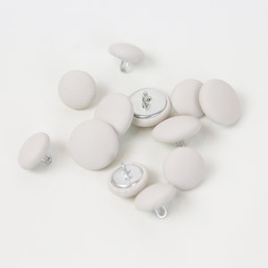 Op de afbeelding: Een groep van tien witte knoppen met zilveren metalen stelen. De knoppen zijn rond en hebben een glad oppervlak.