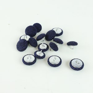 May include: A group of 14 navy blue buttons with silver metal shanks. The buttons have a woven texture and are scattered on a white surface.