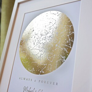 May include: A framed print featuring a circular gold foil star map with white constellations. Below the circle, the text reads ALWAYS & FOREVER followed by the names Michael & Olivia in a cursive script font on a white background.