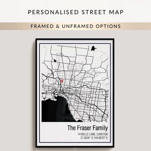 May include: A framed vertical wall art print featuring a black and white street map of a city. The map includes a red location pin icon, the text The Fraser Family, 14 BELLE LANE, CARLTON, and the coordinates 37.8008 S 144.9670 E.