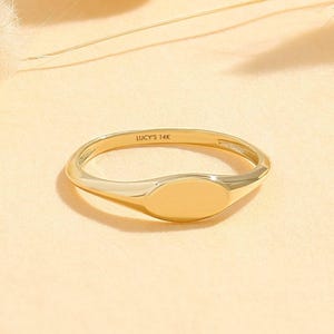 Peut inclure: Une bague chevalière en or avec une face ovale lisse et polie. L'intérieur de l'anneau porte l'inscription gravée LUCY'S 14K. La bague présente un anneau fin et arrondi ainsi qu'une partie supérieure ovale, plate et solide, au fini métallique.