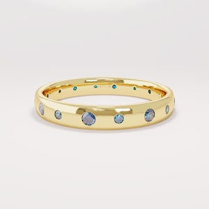 Può includere: Un anello d'oro con più pietre preziose blu incastonate attorno alla fascia. L'anello ha una superficie liscia e lucida e una forma arrotondata. L'anello è un gioiello.