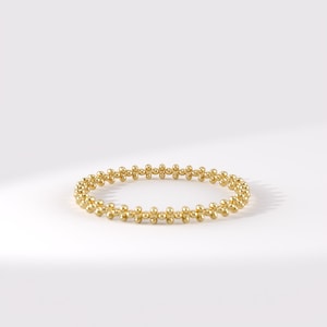 Op de afbeelding: Een gouden ring bestaande uit een doorlopende band van kleine, gepolijste bolvormige kralen in een herhalend patroon. De cirkelvormige band heeft een heldere, reflecterende metalen afwerking en een uniforme structuur met een fijne textuur.