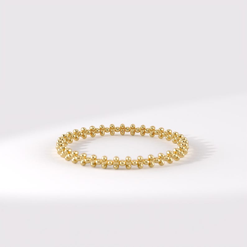 Op de afbeelding: Een gouden ring bestaande uit een doorlopende band van kleine, gepolijste bolvormige kralen in een herhalend patroon. De cirkelvormige band heeft een heldere, reflecterende metalen afwerking en een uniforme structuur met een fijne textuur.