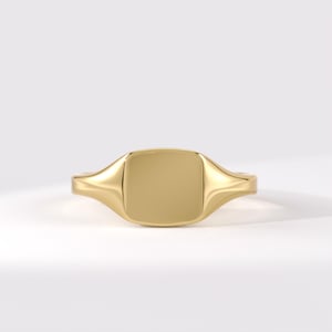 May include: A polished gold signet ring featuring a smooth, flat, square-shaped face with rounded corners. The band tapers slightly as it extends from the central square plate, showcasing a continuous, reflective metallic surface throughout the design.