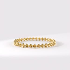 May include: A gold ring featuring a continuous band of small, uniform spherical beads arranged in a repeating pattern. The metallic surface has a polished, reflective finish, creating a circular shape that is consistent in size and texture throughout.