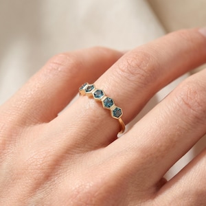 Op de afbeelding: Een gouden ring met vijf kleine, blauwe, zeshoekig geslepen edelstenen op een rij boven op de ringband. De stenen zijn horizontaal geplaatst en elk gevat in een gouden zetting die de zeshoekige vorm van de edelstenen nauwkeurig volgt.