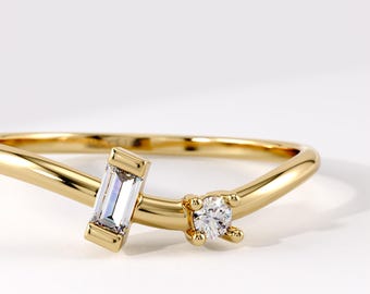 Puede incluir: Un anillo de oro con una banda lisa y curva, engastado con un diamante de corte baguette rectangular y un diamante de corte brillante redondo. Las piedras están situadas en la parte superior de la banda, con un acabado en oro amarillo pulido.