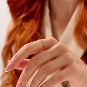 Op de afbeelding: Een dunne gouden ring bestaande uit een doorlopende band van kleine, bolvormige kralen. Het metaal heeft een gepolijste, reflecterende afwerking, wat zorgt voor een delicate en uniforme textuur rondom de gehele omtrek van het sieraad.