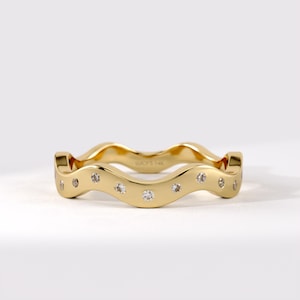May include: A gold wavy band ring featuring a series of small, round, clear stones set along the outer surface. The interior of the band is engraved with the text LUCY'S 14K, indicating the metal purity and brand name on this polished jewelry piece.
