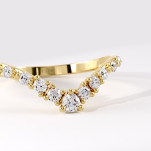 May include: A yellow gold V-shaped ring featuring a series of round, clear, faceted stones set along the band. The metal band has a polished finish and includes a visible hallmark engraving on the inner surface, showcasing a curved design.