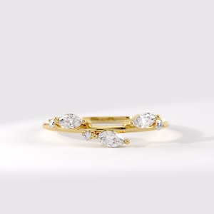May include: A gold ring featuring a thin, polished band adorned with multiple marquise-cut clear stones arranged in an asymmetrical, staggered pattern along the top. The stones are set in small gold prongs, creating a delicate, branch-like appearance.