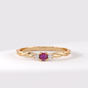 Pode incluir: Um anel de ouro com uma pedra preciosa rosa de corte redondo central ladeada por duas pedras claras menores. A banda tem um design tran&ccedil;ado semelhante a uma corda e est&aacute; gravada com o texto LUCY'S 14K na superf&iacute;cie interna da banda de metal.