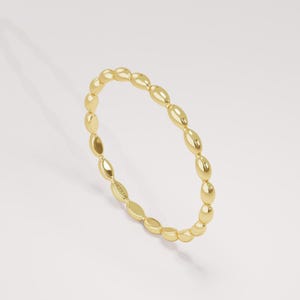 May include: A thin yellow gold ring featuring a continuous band of small, polished, oval-shaped beads. The metal surface is smooth and reflective, catching the light. A small inscription reading LUCY'S 14K is visible on the inner side of the band.