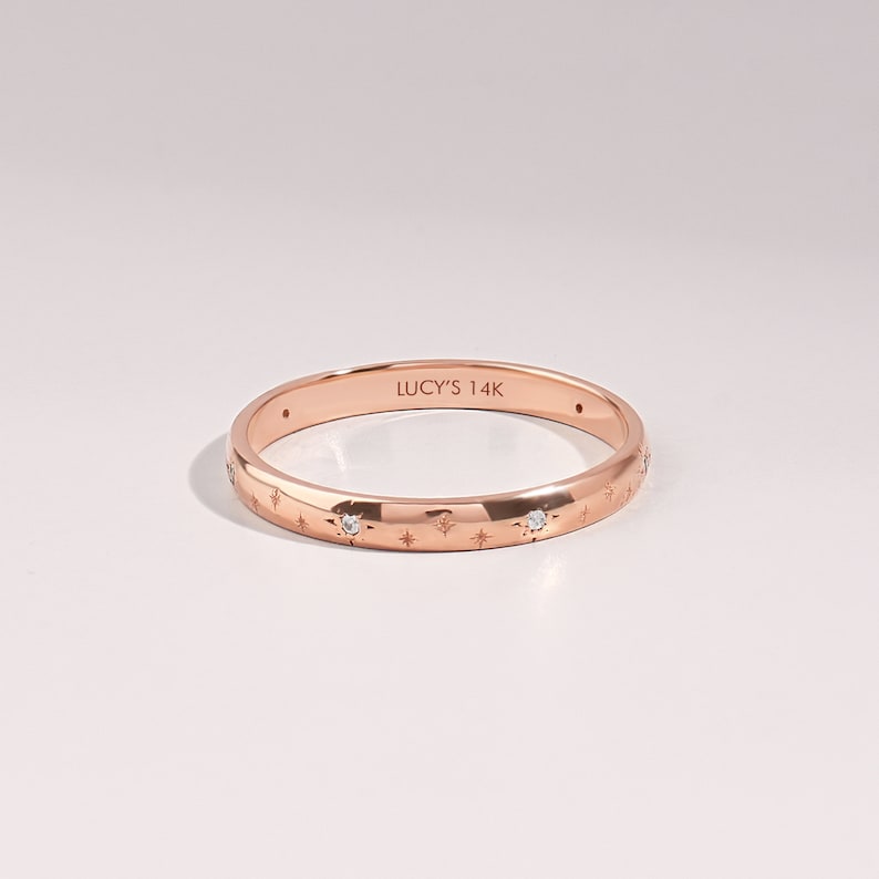 14k solid rose gold 2mm wedding band with engraved with tiny stars and flush setted G Colour SI Clarity genuine diamonds on a white background