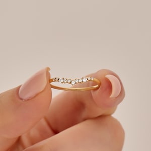 May include: A gold ring with a curved, V-shaped band featuring a cluster of seven small, clear, round-cut stones set along the top. The inner band is engraved with the text LUCY'S 14K, indicating the metal purity of the gold ring.