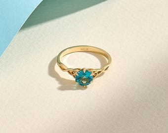 May include: A gold ring featuring a round, faceted blue gemstone set in a prong setting. The band displays an intricate, interwoven metal design on both sides of the stone. The interior of the band is clearly engraved with the text LUCY'S 14K.