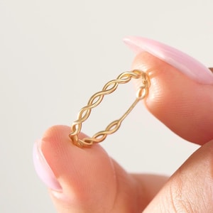 May include: A thin gold ring featuring a continuous twisted rope or infinity-style pattern. The band has a smooth, polished finish and a delicate, lightweight construction, showcasing a repeating interlocking design throughout the entire circumference.