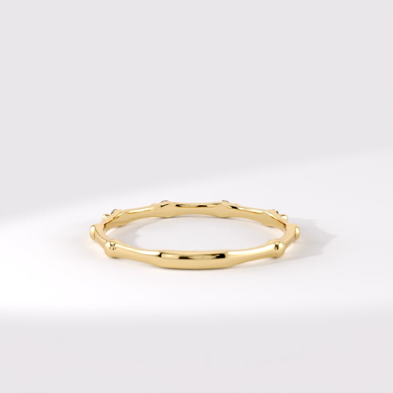 May include: A polished yellow gold ring featuring a continuous bamboo-inspired design with segmented nodes. The band has a smooth, reflective metallic finish and a circular shape, showcasing a uniform structure throughout the entire piece of jewelry.