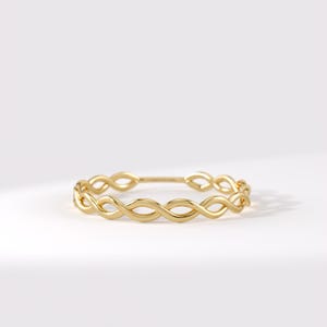 Op de afbeelding: Een ring van gepolijst geelgoud met een doorlopend gedraaid bandontwerp in infinity-stijl. Het metalen oppervlak is glad en reflecterend en vormt een reeks onderling verbonden lussen die een delicate, cirkelvormige bandstructuur creëren.