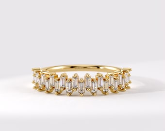 Puede incluir: Un anillo de banda dorada con una serie de piedras transparentes de corte baguette dispuestas en un patrón alterno y escalonado a lo largo de la mitad superior. El metal tiene un acabado pulido y las piedras están fijadas con garras.