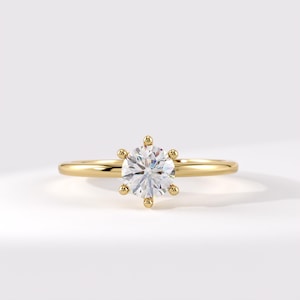 May include: A gold ring featuring a single round brilliant-cut clear gemstone held in a six-prong setting. The band is smooth, polished, and circular, showcasing a classic design with a high-shine metallic finish and a faceted centre stone.
