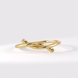 May include: A polished yellow gold ring featuring a bypass design where the two ends of the band overlap. Each terminal end of the gold band is capped with a small, round, clear gemstone, creating a delicate and continuous metallic loop structure.