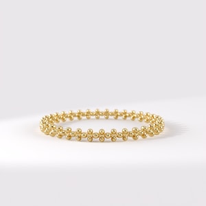 May include: A gold ring featuring a continuous band of small, uniform spherical beads arranged in a repeating pattern. The metallic surface has a polished, reflective finish, creating a circular shape that is consistent in size and texture throughout.