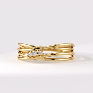 May include: A gold ring featuring a multi-strand crossover design with four polished bands that intersect. Three small, round, clear, brilliant-cut stones are set in a horizontal row on the front, secured by small gold prongs.