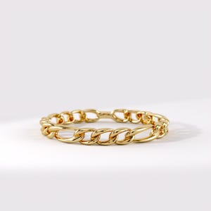 May include: A polished gold-tone ring featuring a continuous curb chain link design. The band is constructed from interconnected oval-shaped metal links that create a uniform, textured appearance with a reflective, high-shine metallic finish.