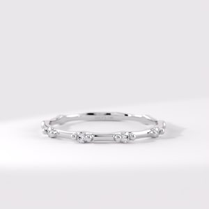 May include: A thin silver-toned metal band ring featuring a series of small, clear, round-cut stones set at intervals. Each stone is flanked by two tiny metal spheres, creating a repeating pattern along the circumference of the circular ring.