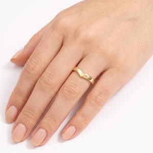 May include: A polished gold band ring featuring a V-shaped chevron design. The ring has a smooth, reflective surface and a continuous metal construction, worn on the ring finger. The design is simple, featuring a pointed center peak.