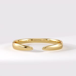 May include: A polished gold open cuff bracelet with a smooth, rounded surface. The band features a tapered design that narrows toward the two open ends, creating a sleek, continuous loop with a reflective metallic finish and a minimalist aesthetic.