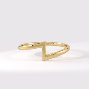 Könnte beinhalten: Ein polierter Goldring mit einem zentralen geometrischen Blitz- oder Zickzack-Motiv. Das Band ist glatt und durchgehend, wobei die kantige Form in das kreisförmige Design integriert ist, was ein glattes, metallisches und reflektierendes Aussehen erzeugt.
