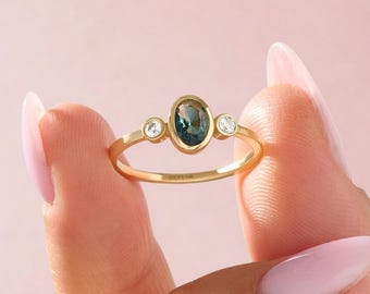 May include: A gold ring featuring a central oval-cut teal gemstone in a bezel setting, flanked by two smaller round-cut clear stones. The inner band is engraved with the text LUCY'S 14K, indicating the metal composition of this jewelry piece.