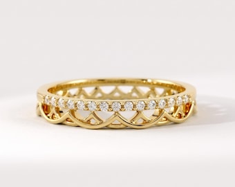 May include: A gold ring featuring a band set with a row of small, clear, round-cut stones. The band has a decorative, scalloped, open-work design along the lower edge, creating a layered appearance with a polished, reflective metallic finish.