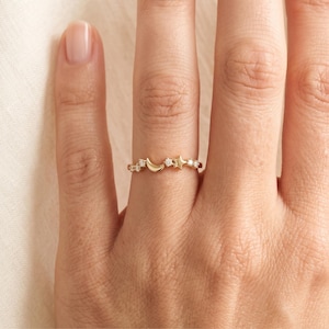 May include: A gold ring featuring a delicate band adorned with a small crescent moon, a five-pointed star, and several tiny round clear stones arranged in a row along the top section of the metal band, creating a celestial-inspired design.