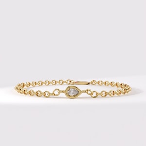 May include: A gold chain bracelet featuring a single pear-shaped diamond set in a gold bezel. The bracelet is constructed from a series of small, round, interlocking gold links that form a continuous circular band around the central gemstone.